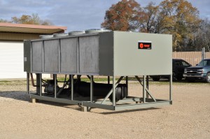 Large outdoor Trane industrial chiller unit on gravel, showcasing reliable Industrial & Commercial Chillers with trees and vehicles in the background.